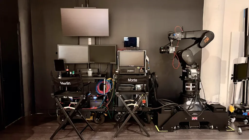 A load of high-end studio equipment up against the wall, includes monitors, robot arm, seats, control systems, etc.